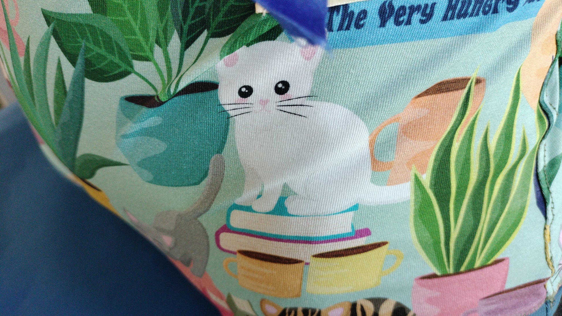 A section of the fabric design with a white cat, houseplants & books